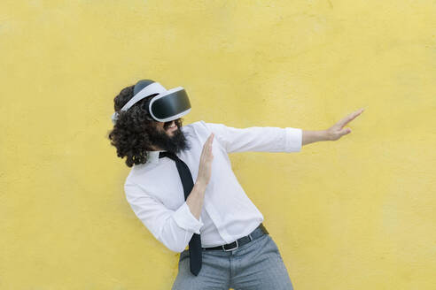 Mann mit Virtual-Reality-Brille gestikuliert Stoppschild, während er an der Wand steht - MRRF00556