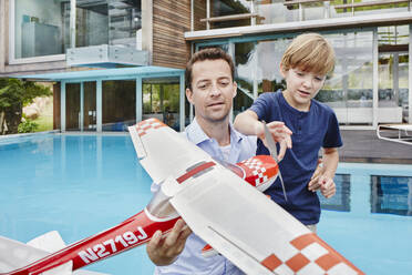 Vater und Sohn spielen mit einem Spielzeugflugzeug, während sie am Schwimmbecken stehen - RORF02333