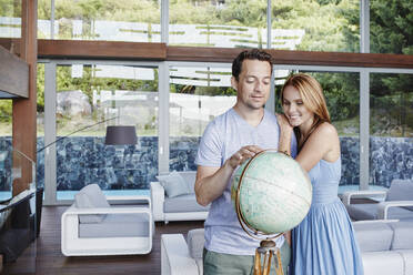 Couple looking at globe while standing in modern house - RORF02340