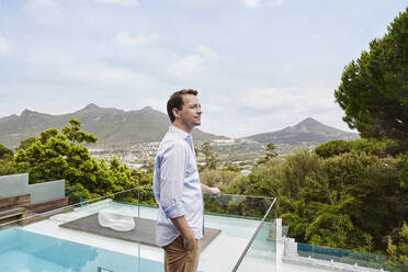 Mature man with hands in pockets looking away while standing in balcony - RORF02345