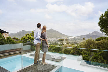 Heterosexual couple standing while looking at view from balcony of modern house - RORF02346