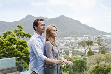 Heterosexual couple holding wine glass looking away while standing in balcony - RORF02351