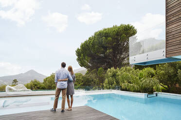 Heterosexual couple looking at view while standing near swimming pool - RORF02353