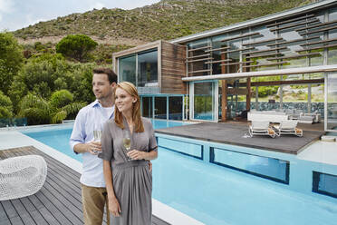 Paar hält Weinglas, während es vor einem modernen Haus steht - RORF02357