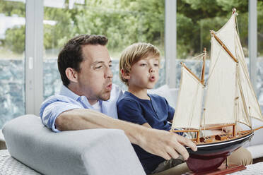 Vater und Sohn blasen Spielzeugboot, während sie zu Hause sitzen - RORF02383