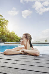 Junge Frau schaut weg, während sie an einem sonnigen Tag im Pool liegt - RORF02405