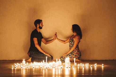 Couple touching hands while kneeling by lit candles in darkroom at home - DLTSF01338