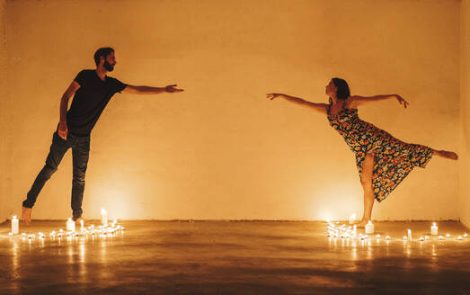 Couple stretching arms to reach while standing amidst lit candles in darkroom - DLTSF01339
