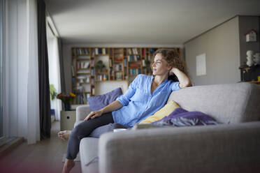 Woman with head in hands resting while sitting on sofa at home - RBF07946