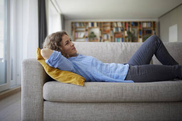 Woman with hands behind head lying on sofa at home - RBF07957