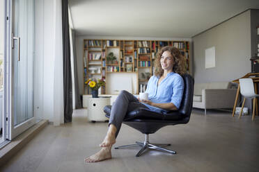 Smiling woman drinking coffee while sitting on chair at home - RBF07961