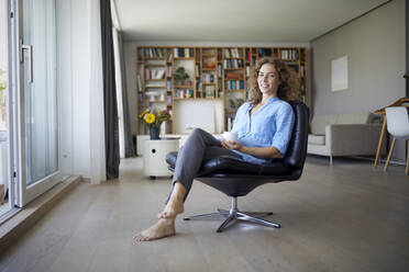 Mid adult woman drinking coffee while sitting on chair at home - RBF07963