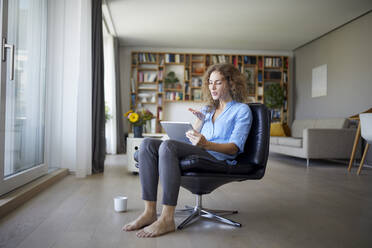 Woman blowing kiss to video call on digital tablet while sitting on chair at home - RBF07966