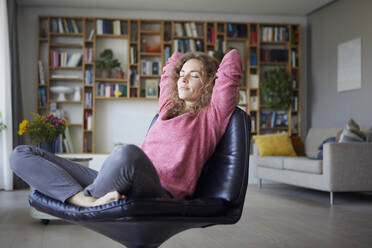 Mittlere erwachsene Frau mit Händen hinter dem Kopf entspannt auf einem Stuhl zu Hause - RBF07971