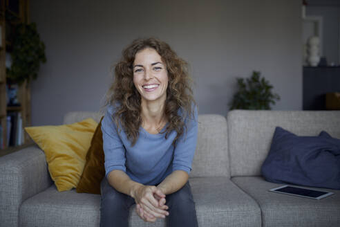 Schöne Frau lächelt, während sie zu Hause auf dem Sofa sitzt - RBF07980