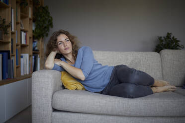 Woman with head in hands lying on sofa at home - RBF07982