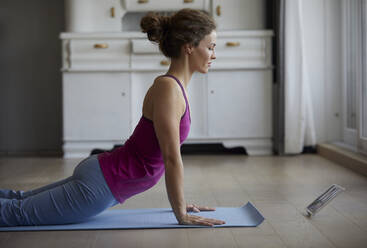 Mittlere erwachsene Frau, die beim Yoga zu Hause auf ein digitales Tablet schaut - RBF07993