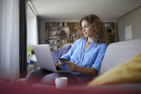 Smiling woman doing online shopping on laptop at home - RBF07998
