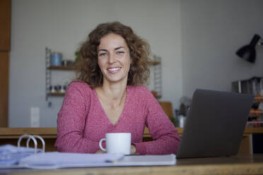 Smiling woman using laptop while working at home - RBF08009