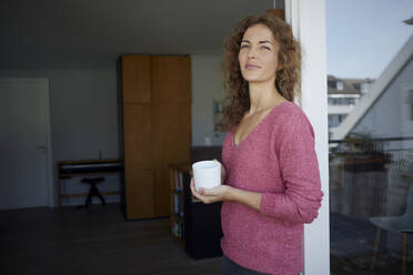 Lächelnde Frau, die Kaffee trinkt und sich zu Hause an die Tür lehnt - RBF08012