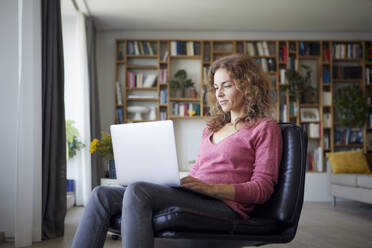 Frau benutzt Laptop, während sie zu Hause auf einem Stuhl sitzt - RBF08022