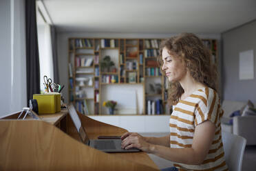 Frau arbeitet am Laptop, während sie zu Hause am Schreibtisch sitzt - RBF08026