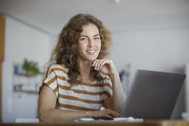 Smiling mid adult woman using laptop while sitting at home - RBF08036