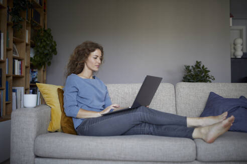 Frau arbeitet am Laptop, während sie zu Hause auf dem Sofa sitzt - RBF08043