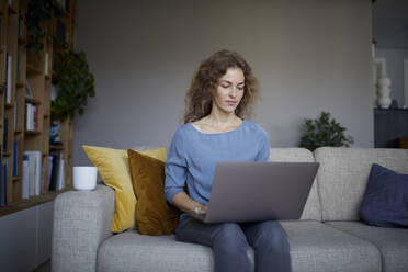Frau sitzt auf dem Sofa und arbeitet zu Hause am Laptop - RBF08045