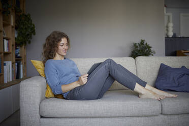 Smiling woman using digital tablet while sitting on sofa at home - RBF08048