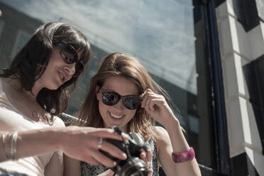 Lächelnde Frau schaut in die Kamera, die von einer Freundin in der Stadt an einem sonnigen Tag gehalten wird - AJOF00178