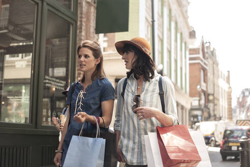Schöne Freundinnen unterhalten sich beim Spaziergang mit Einkaufstaschen in der Stadt - AJOF00182