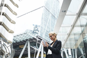 Beautiful female professional using smart phone while standing against office building at downtown district - PMF01292