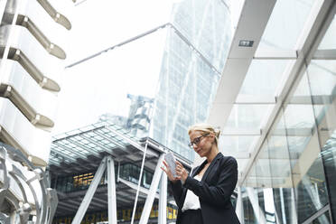 Schöne weibliche Fachkraft, die ein Smartphone benutzt, während sie vor einem Bürogebäude in der Innenstadt steht - PMF01292