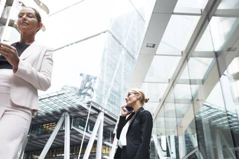 Mature female entrepreneur talking on mobile phone while standing near businesswoman in downtown district stock photo