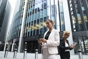 Reife Geschäftsfrauen mit Smartphones gegen moderne Büro-Wolkenkratzer im Stadtzentrum - PMF01296