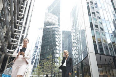 Businesswomen using mobile phones against office buildings in city - PMF01306