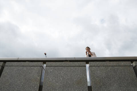 Businesswoman talking through smart phone while standing on footbridge at downtown district stock photo