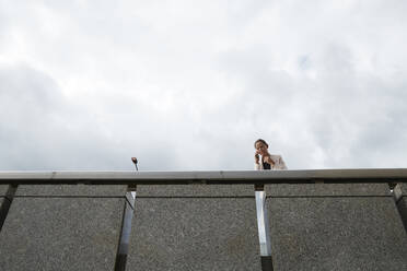 Geschäftsfrau, die über ihr Smartphone spricht, während sie auf einer Fußgängerbrücke im Stadtzentrum steht - PMF01319