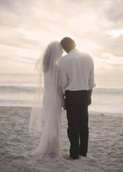 Neuvermähltes Paar steht am Strand bei Sonnenuntergang - AJOF00186