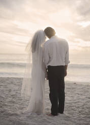 Newlywed couple standing at beach during sunset - AJOF00186