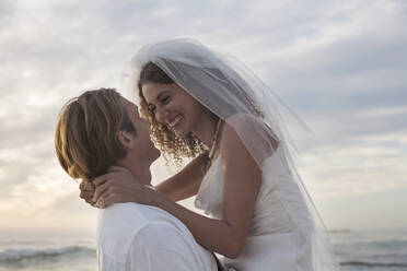 Romantic newlyweds at beach against sky during sunset - AJOF00188