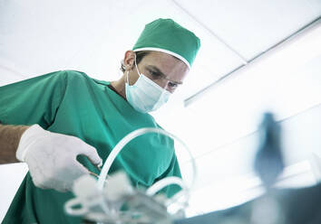 Männlicher Chirurg, der in der beleuchteten Intensivstation eines Krankenhauses operiert - AJOF00200