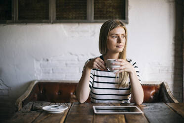 Frau schaut weg und trinkt eine Tasse Kaffee, während sie in einem Cafe sitzt - ABZF03402