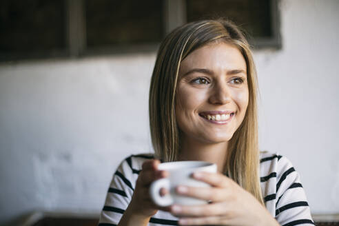 Lächelnde Frau schaut weg, während sie in einem Café Kaffee trinkt - ABZF03404