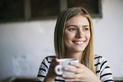 Smiling woman looking away while drinking coffee in cafe - ABZF03404