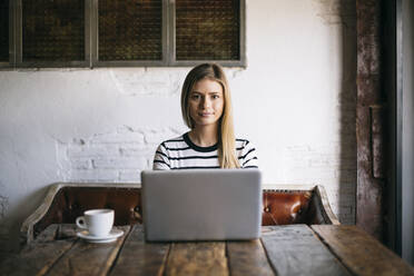 Woman using laptop while sitting in cafe - ABZF03407