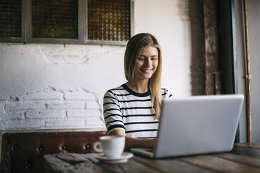 Mid adult woman smiling while using laptop in cafe - ABZF03408