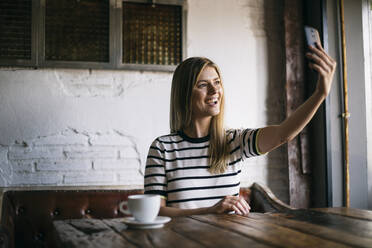 Beautiful woman taking selfie on smart phone while sitting in cafe - ABZF03411