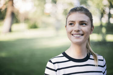 Smiling woman looking away while standing in public park - ABZF03415